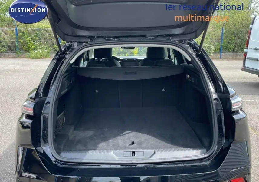 Vue arrière ouverte du coffre spacieux d'une Peugeot 308 SW Hybrid 145ch noire métal, avec hayon relevé en extérieur.