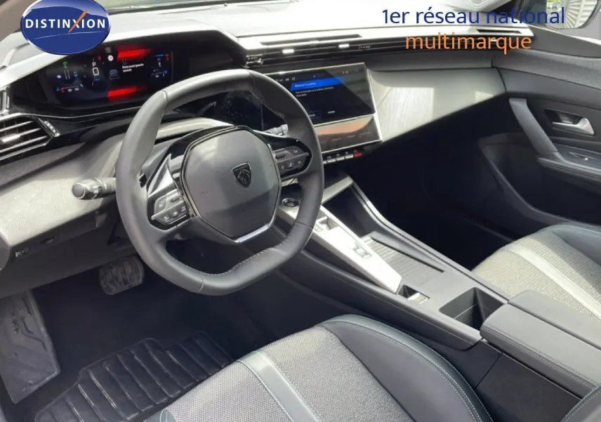 Vue intérieure du poste de conduite de la Peugeot 308 SW Hybrid 2025, avec volant cuir noir et écran tactile central.