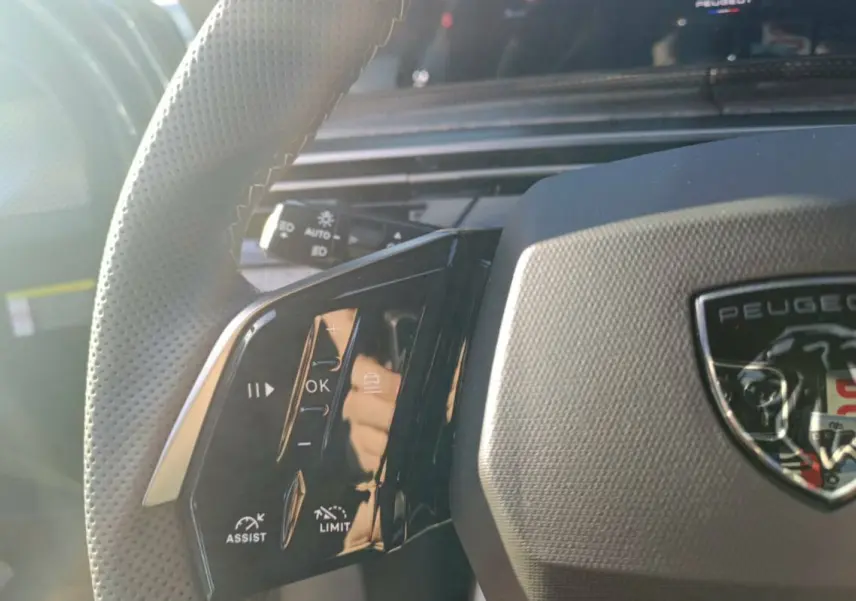 Gros plan sur le volant cuir perforé côté gauche du Peugeot 3008 Hybrid bleu ingaro avec commandes multifonctions.