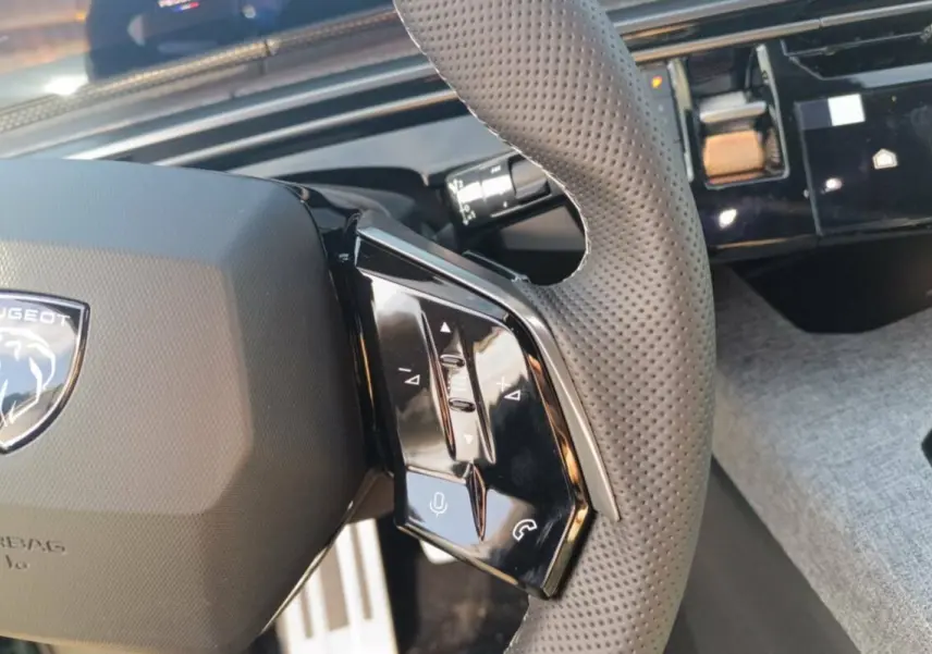 Gros plan sur le volant cuir perforé du Peugeot 3008 Hybrid 2025, avec commandes multifonctions et tableau de bord noir.