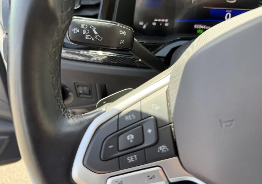 Gros plan sur le volant noir et les commandes multifonctions du Volkswagen Taigo 1.0 TSI 110CH DSG Life, tableau de bord en arrière-plan.