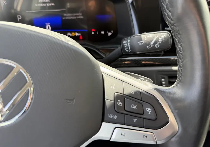 Gros plan sur le volant cuir noir du Volkswagen Taigo 2022 avec commandes intégrées et tableau de bord numérique en arrière-plan.