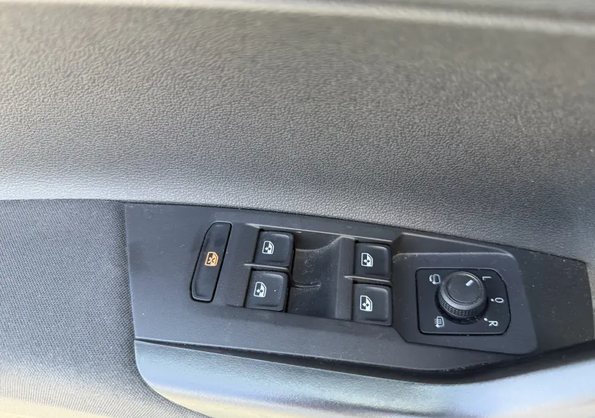 Vue rapprochée des commandes de lève-vitres et réglage des rétroviseurs sur la porte côté conducteur d’un Volkswagen Taigo gris.
