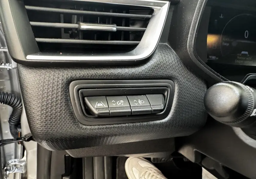 Gros plan sur les commandes de réglage d'assistance et phares à gauche du tableau de bord gris clair de la Renault Clio Business E-TECH 2022.