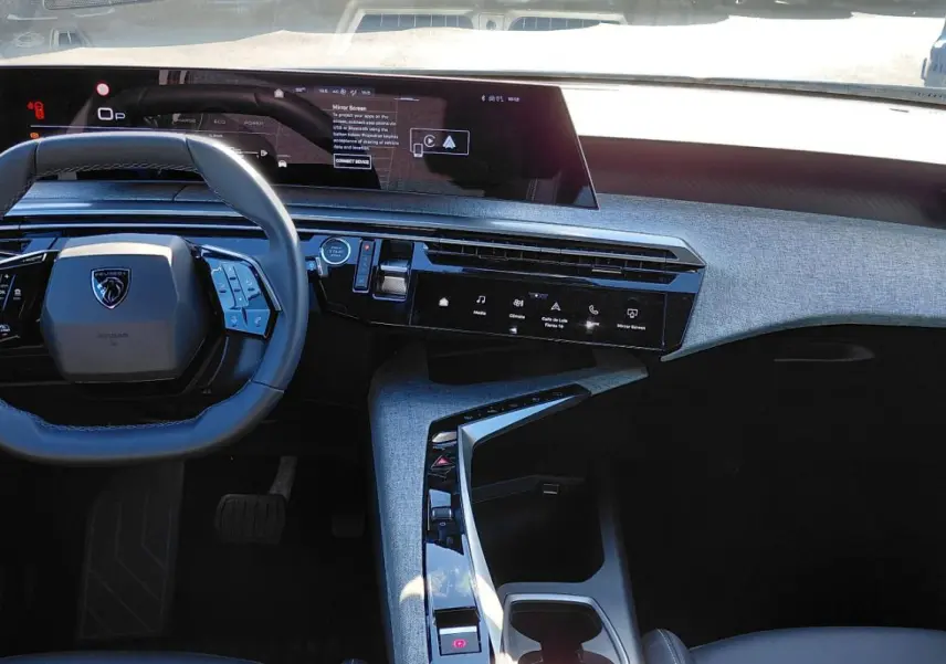 Vue intérieure du tableau de bord et volant du Peugeot 5008 Hybrid 2025 avec écran numérique large et finition tissu gris.