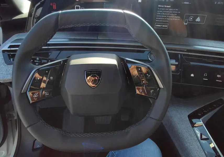 Vue intérieure centrée sur le volant noir du Peugeot 5008 Hybrid 2025 avec tableau de bord numérique et habillage gris.