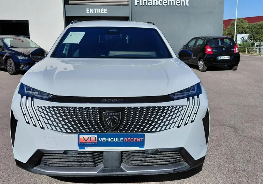 Vue avant d’un Peugeot 5008 blanc 2025 avec calandre distinctive et phares LED verticaux, stationné en extérieur.