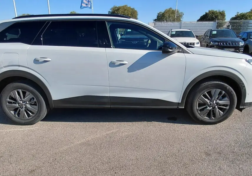 Peugeot 5008 Hybrid blanc vue de profil côté gauche, avec jantes alliage et vitres teintées, stationné en extérieur.