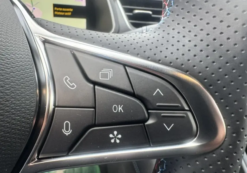 Gros plan sur les commandes noires du volant perforé de la Renault Symbioz gris Cassiopée, avec surpiqûres bleues.