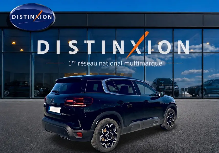 Vue 3/4 arrière droite d'un Citroën C5 Aircross noir 2024 avec jantes alu et barres de toit devant un bâtiment Distinxion.