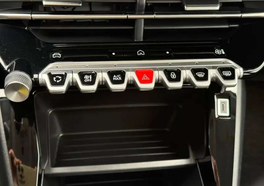 Vue rapprochée de la console centrale noire du Peugeot 208 1.2 Hybrid, avec boutons argentés et bouton rouge d’alerte.
