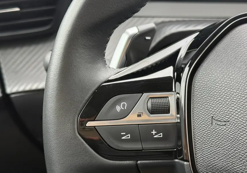 Gros plan sur les commandes vocales et volume sur le volant noir de la Peugeot 208 hybride 2025.
