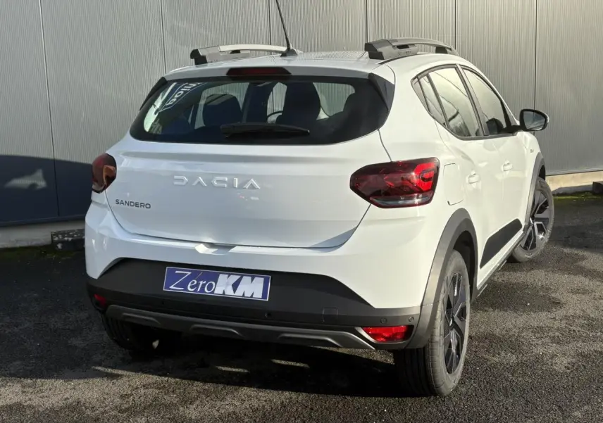 Vue 3/4 arrière droite du Dacia Sandero Stepway blanc glacier avec barres de toit et jantes noires.