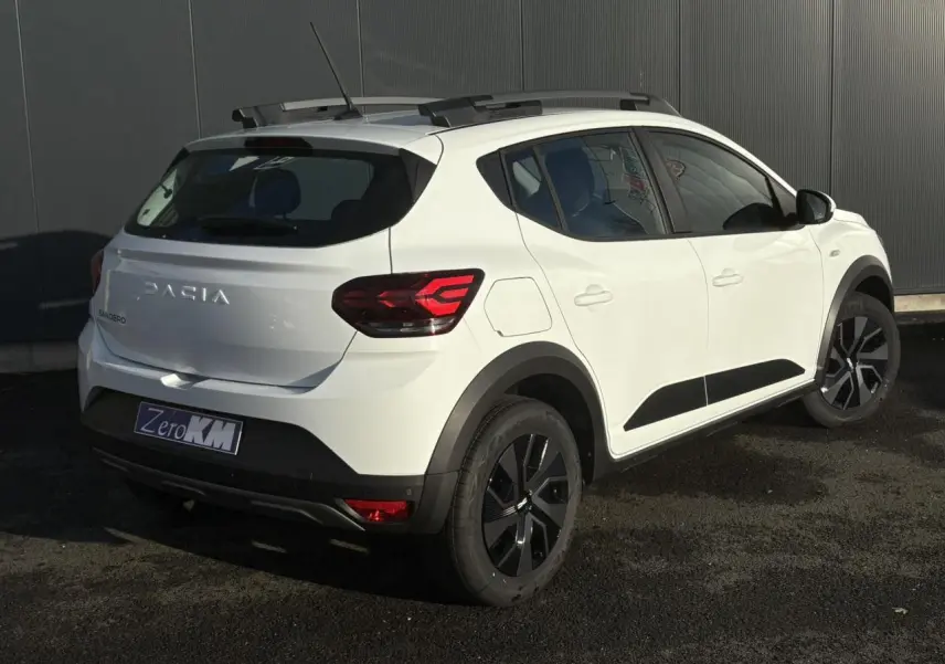 Vue 3/4 arrière droite d'une Dacia Sandero Stepway blanche Glacier avec barres de toit et feux LED distinctifs.