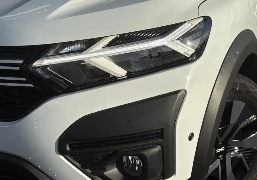 Gros plan sur l'avant droit blanc glacier du Dacia Sandero Stepway 2024, mettant en valeur le phare LED et la roue noire.
