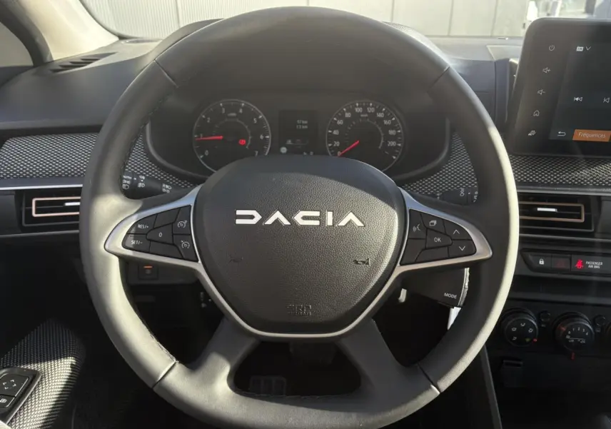 Vue rapprochée du volant noir de la Dacia Sandero Stepway 2024 avec commandes intégrées et tableau de bord visible.
