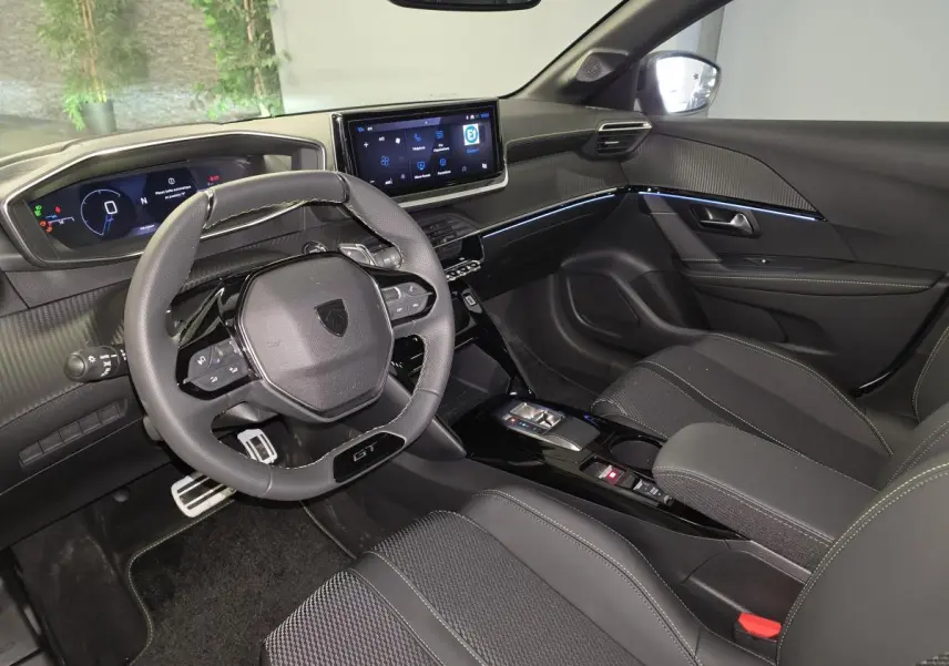 Intérieur avant droit de la Peugeot 208 GT 2025 avec volant cuir, écran tactile et sellerie tissu noire.