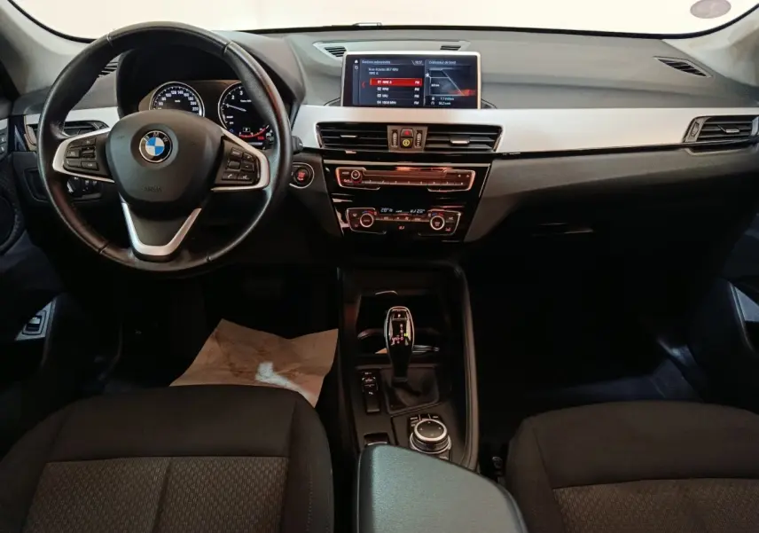 Vue intérieure avant de la BMW X1 sDrive18i 2021, tableau de bord noir avec écran central et volant cuir multifonctions.