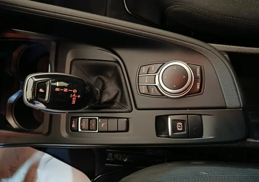 Vue rapprochée de la console centrale noire du BMW X1 sDrive18i Lounge avec levier de vitesses automatique et molette de contrôle.