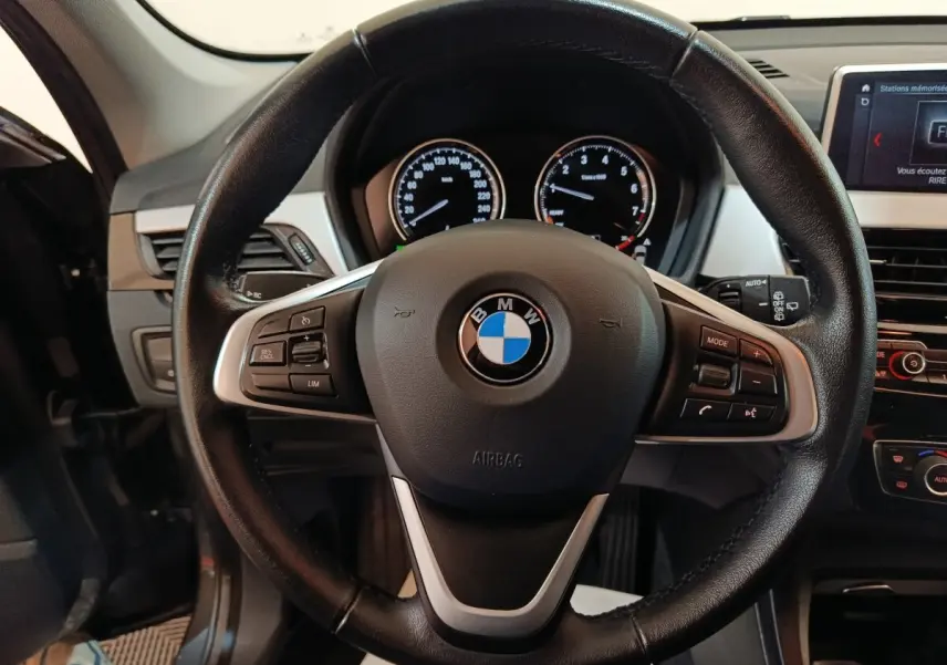 Vue rapprochée du volant cuir noir multifonctions d’un BMW X1 2021, avec tableau de bord et écran digital visibles.