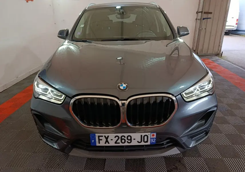 Vue avant d’un BMW X1 sDrive18i Lounge gris foncé avec calandre double haricot et phares LED allumés dans un garage.