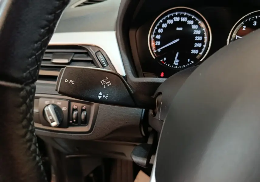 Gros plan sur la commande de clignotant et le tableau de bord noir d'une BMW X1 sDrive18i Lounge 2021.