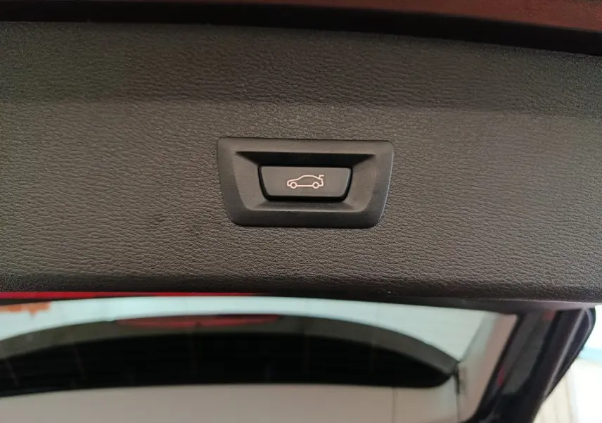 Bouton de fermeture électrique du coffre visible sur la partie intérieure du hayon d’un BMW X1 gris foncé.
