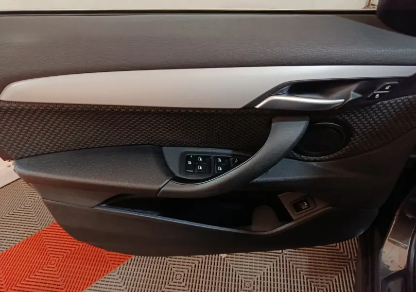 Vue rapprochée de la porte avant gauche du BMW X1 gris foncé, avec commandes de vitres et poignée argentée.