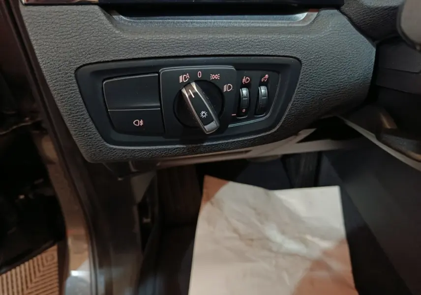 Gros plan sur les commandes d'éclairage du tableau de bord d'un BMW X1 sDrive18i Lounge gris foncé, côté conducteur.