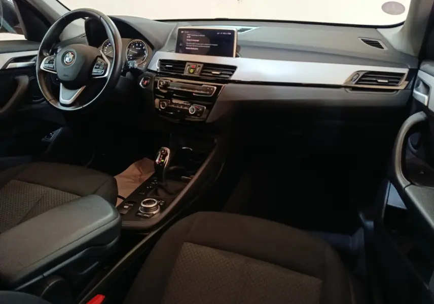 Intérieur BMW X1 sDrive18i 2021 vu côté conducteur, tableau de bord noir avec écran central et volant cuir multifonctions.