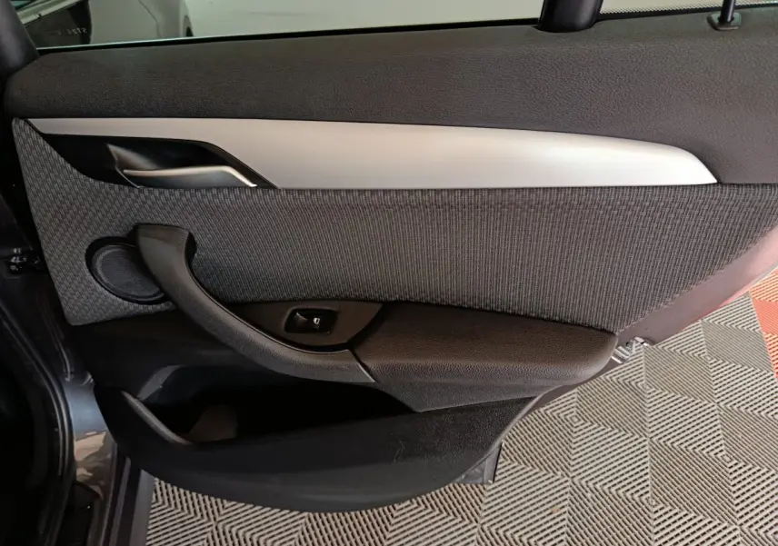 Gros plan sur la porte arrière gauche intérieure du BMW X1 sDrive18i Lounge 2021, avec garniture grise et poignée noire.