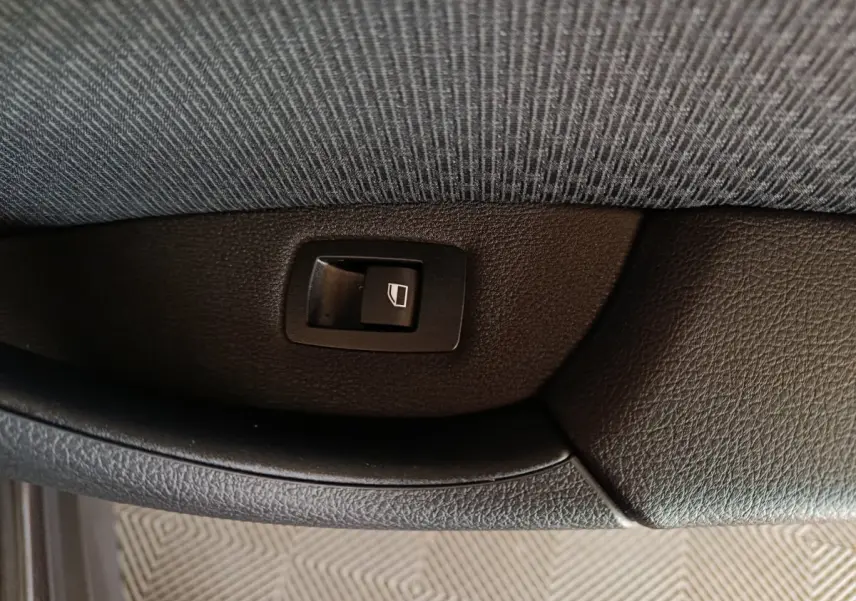 Gros plan sur l'interrupteur de lève-vitre côté porte intérieure d'une BMW X1 gris foncé sDrive18i Lounge 2021.