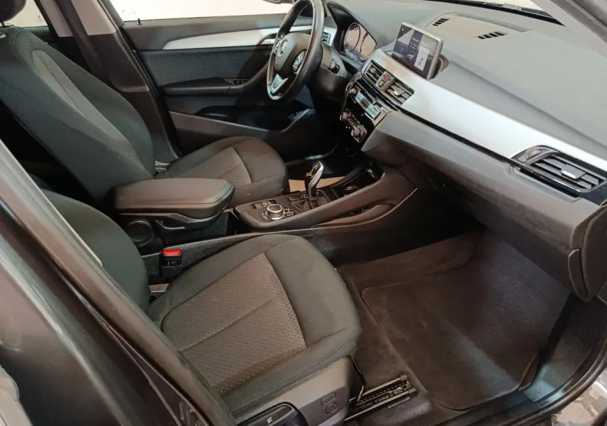 Intérieur avant de la BMW X1 sDrive18i Lounge 2021, vue côté conducteur, sièges tissu gris et tableau de bord moderne.