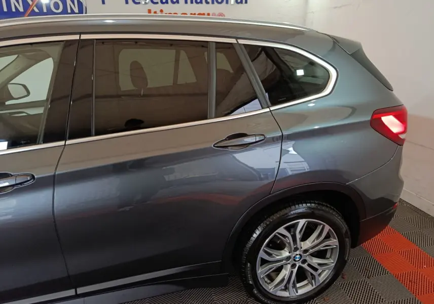 Vue latérale droite sur l'arrière d'un BMW X1 sDrive18i Lounge gris foncé avec feu arrière allumé et jante alliage.