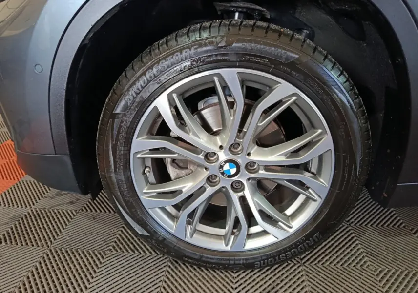 Gros plan sur la roue avant gauche d’un BMW X1 gris foncé avec jante alliage et pneu Bridgestone.