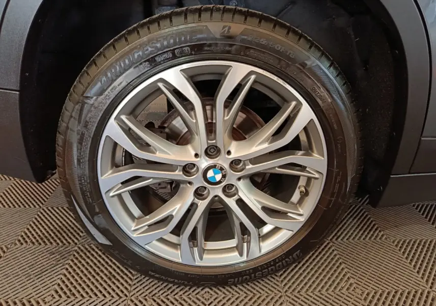 Gros plan sur la roue avant droite d’un BMW X1 gris foncé, montrant le pneu Bridgestone et l’aile du véhicule.