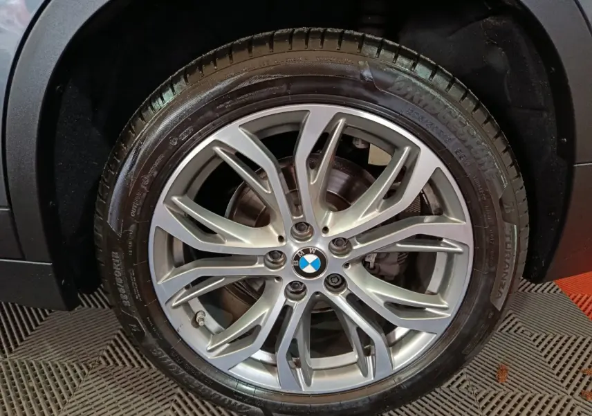 Gros plan sur la roue avant droite d'une BMW X1 gris foncé, mettant en valeur la jante alliage à dix branches.