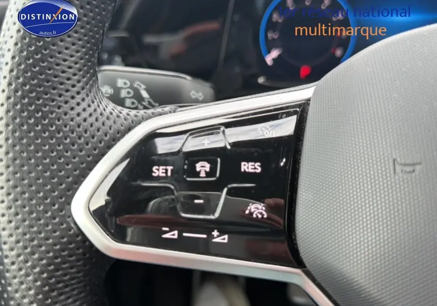 Gros plan sur les commandes multifonctions noires à gauche du volant perforé gris d’une Volkswagen Golf bleue 2024.