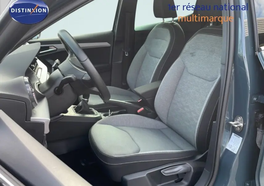 Vue intérieure côté conducteur de la SEAT IBIZA bleu Fjord 2025, sièges tissu gris et volant cuir multifonction.