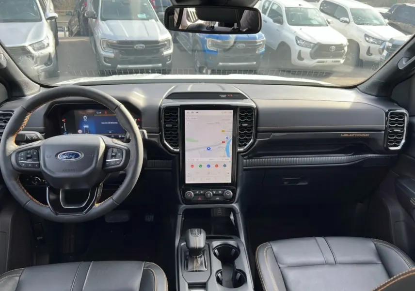 Vue intérieure frontale du Ford Ranger Wildtrak 2025, tableau de bord noir avec écran tactile vertical et volant cuir multifonctions.