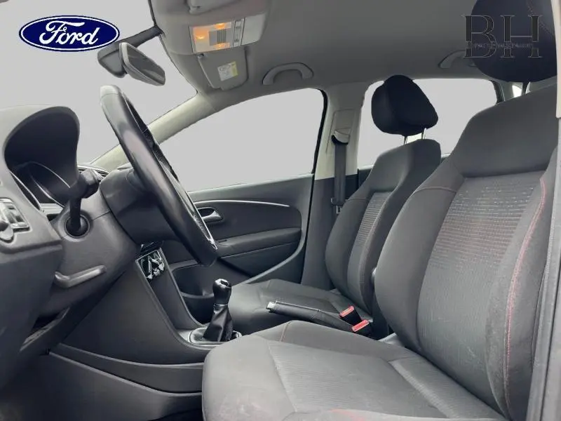 Vue intérieure côté conducteur d'une Volkswagen Polo 1.4 TDI noire, montrant sièges tissu gris et volant cuir multifonction.