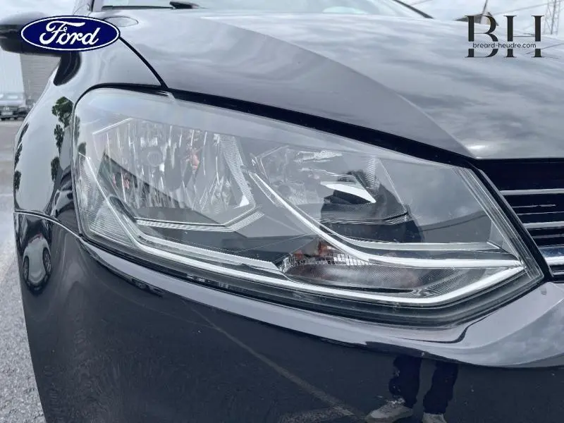 Gros plan sur le phare avant gauche d'une Volkswagen Polo noire 2017, soulignant les détails du bloc optique.