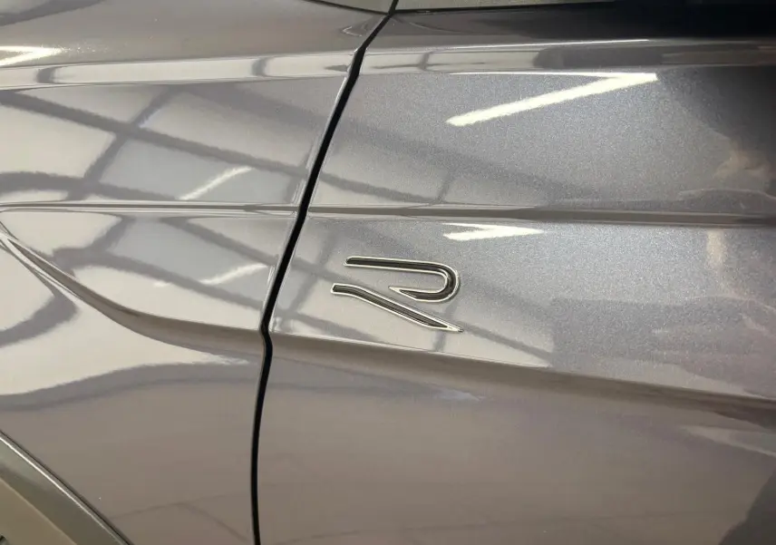Gros plan sur l'emblème R sur la porte avant gauche du Volkswagen Taigo gris cendré métallisé.