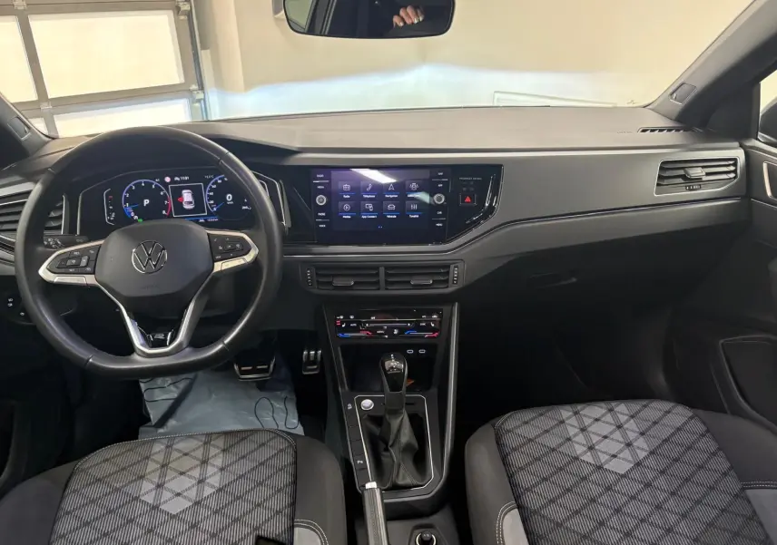 Vue intérieure avant du Volkswagen Taigo 1.5 TSI R-Line 2024, tableau de bord noir avec écran tactile et volant multifonction.