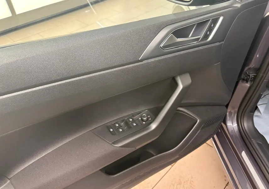 Vue rapprochée de la porte avant gauche du Volkswagen Taigo gris cendré, montrant les commandes des vitres et le verrouillage.
