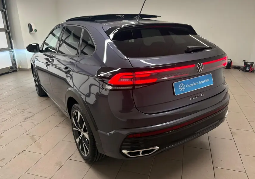 Volkswagen Taigo gris cendré en 3/4 arrière droit, avec feux arrière allumés et jantes noires brillantes.
