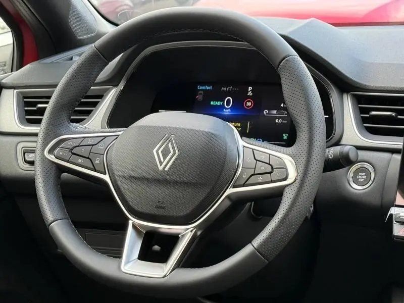 Vue rapprochée du volant multifonction noir du Renault Captur rouge 2025 avec tableau de bord digital et bouton start/stop visible.