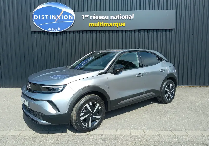 Vue 3/4 avant droite d'un Opel Mokka électrique gris 2025, avec jantes stylisées et calandre noire lisse.