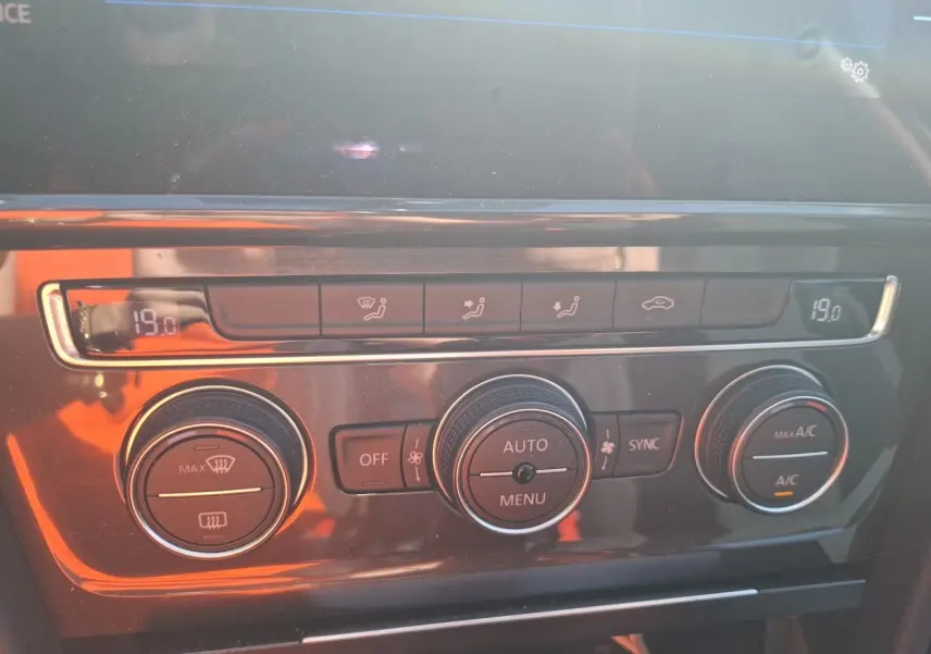 Gros plan sur la console centrale de la Volkswagen Golf blanche, montrant la climatisation automatique bi-zone à 19°C.