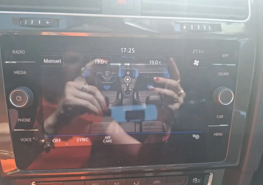 Écran tactile central de la Volkswagen Golf 2019 montrant la climatisation bi-zone avec reflet des mains au-dessus.